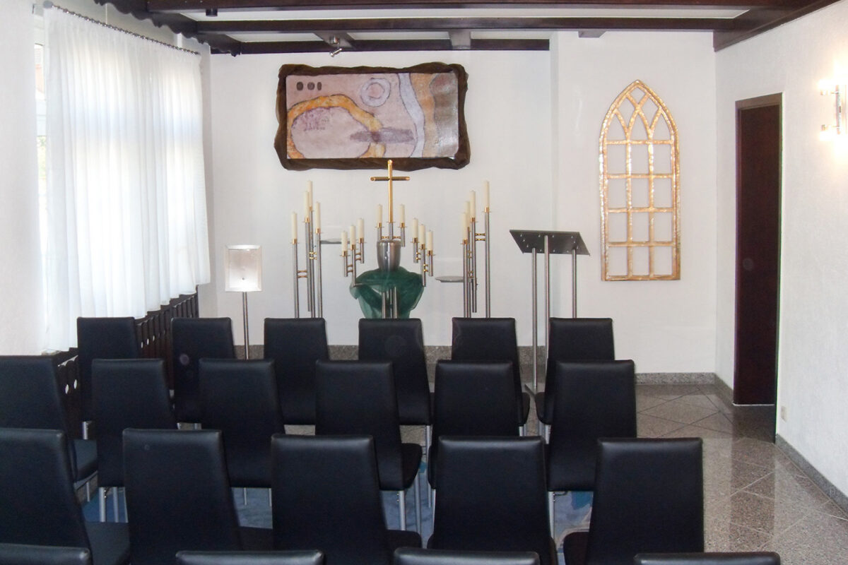 Ruhiger Abschiedsraum mit Altar, Kerzen und Stuhlreihen – würdevoller Rahmen für Urnentrauerfeiern